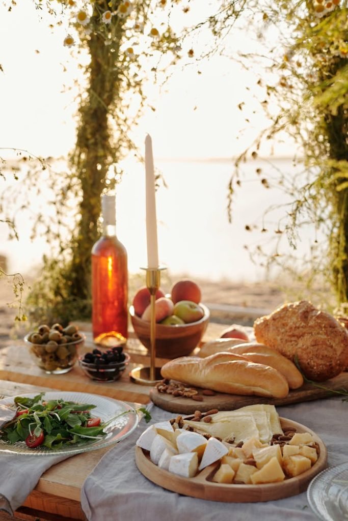 an-assorted-food-on-the-table-5086971 Serene outdoor picnic setup with cheese, wine, and breads on a rustic table at sunset.